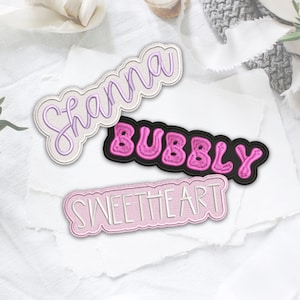 May include: Three embroidered iron-on patches with pink and white thread. The patches read "Shanna", "Bubbly", and "Sweetheart".