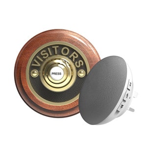 May include: A wooden doorbell with a brass button that says "PRESS" and a black and gold plaque that says "VISITORS". A white and grey wireless doorbell chime is next to the doorbell.