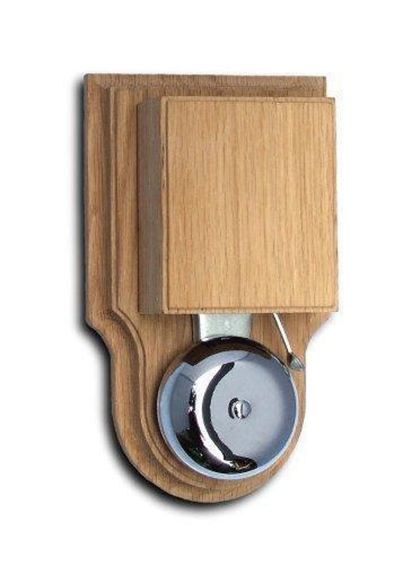 May include: A wooden doorbell with a polished chrome bell. The doorbell is mounted on a wooden plaque with a decorative border.