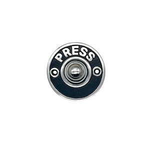 Puede incluir: Un botón de timbre negro y plateado con la palabra "PRESS" en letras blancas.
