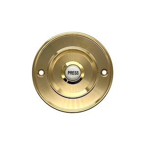 May include: A round, gold-coloured doorbell button with a white, circular button that says "PRESS" in black lettering.