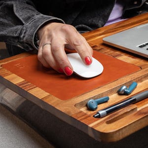 Può includere: Un supporto per laptop in legno con un tappetino per mouse in pelle, una penna e due auricolari wireless. Il supporto ha una scanalatura per tenere un telefono o un tablet.