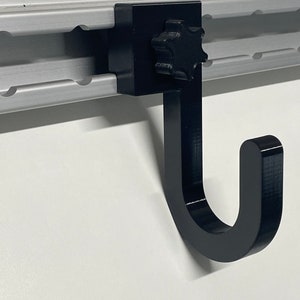 May include: Black plastic hook with a star-shaped knob for mounting on a track system. The hook is designed to hang items on a wall or other surface.