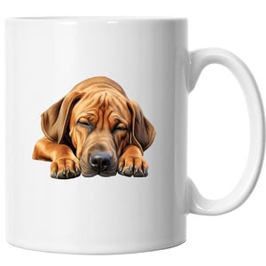 Könnte beinhalten: Weiße Keramiktasse mit einer detaillierten Illustration eines schlafenden braunen Hundes. Der Hund liegt mit geschlossenen Augen, Pfoten nach vorne und Kopf auf den Pfoten. Die Tasse hat einen Standardgriff.