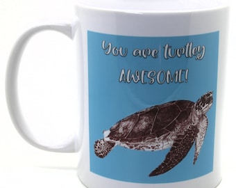 Może przedstawiać: Biały kubek ceramiczny z niebieskim tłem i ilustracją brązowej żółwia morskiego. Tekst "You are turtley AWESOME!" jest nadrukowany na kubku czarnym kolorem.