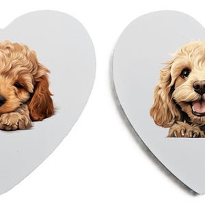May include: Two heart-shaped decorations with illustrations of a Cavalier King Charles Spaniel puppy. One shows the puppy sleeping, the other shows the puppy smiling. The puppies have brown and tan fur.