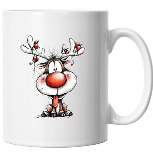 Könnte beinhalten: Weißer Keramikbecher mit einem Cartoon-Rentier-Design. Das Rentier hat eine große rote Nase, rosige Wangen und eine herausgestreckte Zunge. Seine Geweihe sind mit roten Ornamenten verziert, was eine festliche und verspielte Ästhetik erzeugt.