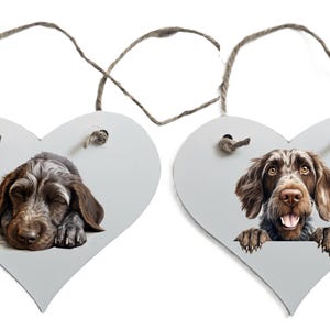 May include: Two heart-shaped wooden ornaments featuring dog portraits. One shows a sleeping dog with brown and grey fur, the other a happy dog with brown fur. Both have twine hangers.