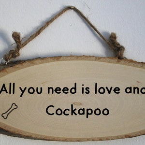 Peut inclure: Panneau ovale en bois avec le texte "All you need is love and a Cockapoo" en noir. Un os et une empreinte de patte sont également présents. Le panneau est suspendu par une corde en ficelle naturelle.