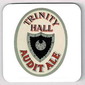 May include: A vintage-style beer coaster with a green and white oval design. The text "Trinity Hall Audit Ale" is printed in red and black lettering. A black and gray shield with a crescent moon design is in the center.