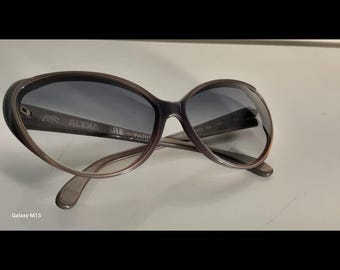 May include: Oversized sunglasses with a dark brown frame and gradient lenses. The brand name "ALEXANDRE PARIS" is visible on the left arm. The glasses have a rounded shape and a light brown gradient on the lower part of the frame.