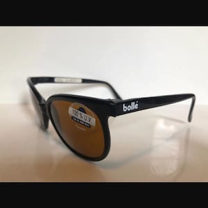 May include: Black sunglasses with brown lenses. The glasses have the brand name "bollé" on the arm and a sticker that reads "100% U.V. Up to 400 Nm France". The frames are black.