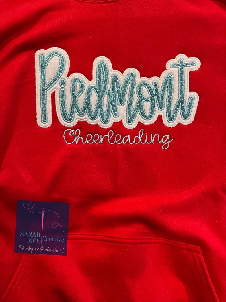 May include: Red hooded sweatshirt with a white and teal blue embroidered design that says "Piedmont Cheerleading".