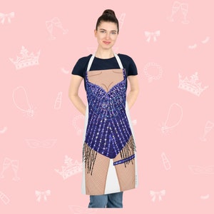 May include: A white apron with a blue sequined design of a woman's body. The apron has a white background and a blue sequined design of a woman's body. The design includes a blue sequined bodice, a blue sequined skirt, and a pair of brown legs. The apron is being worn by a person.