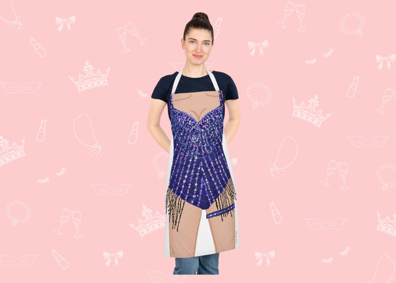 May include: A white apron with a blue sequined design of a woman's body. The apron has a white background and a blue sequined design of a woman's body. The design includes a blue sequined bodice, a blue sequined skirt, and a pair of brown legs. The apron is being worn by a person.