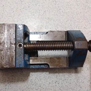 May include: A blue and silver Stanley vise, a tool used to hold workpieces. The vise has a screw mechanism for clamping and a handle for tightening. The word "STANLEY" is visible on the side.