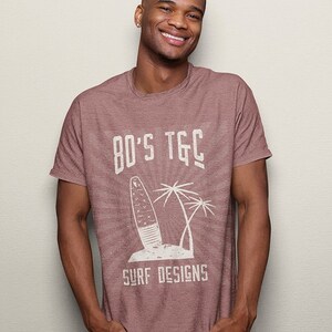 May include: A maroon heather t-shirt with a white graphic design of a surfboard, palm trees, and the text "80's TGC Surf Designs".