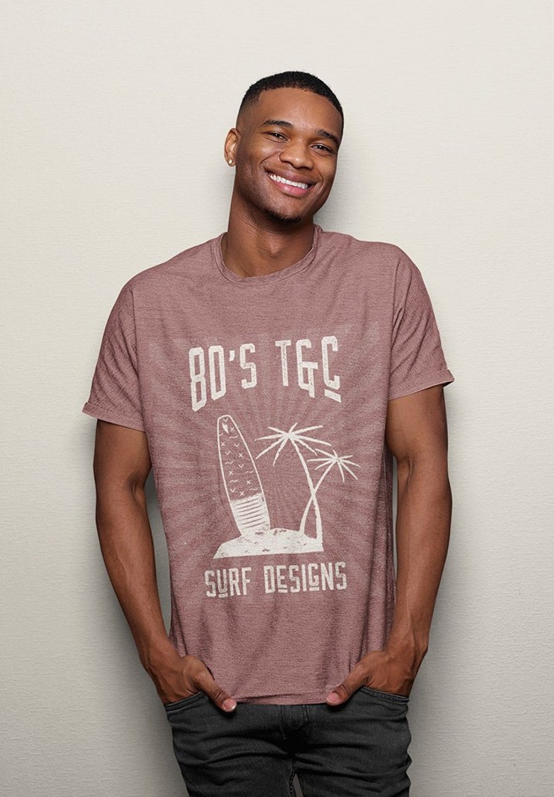 May include: A maroon heather t-shirt with a white graphic design of a surfboard, palm trees, and the text "80's TGC Surf Designs".