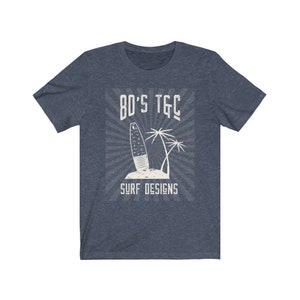 May include: A navy blue t-shirt with a white graphic design of a surfboard and palm trees. The graphic includes the text "80's TGC Surf Designs".
