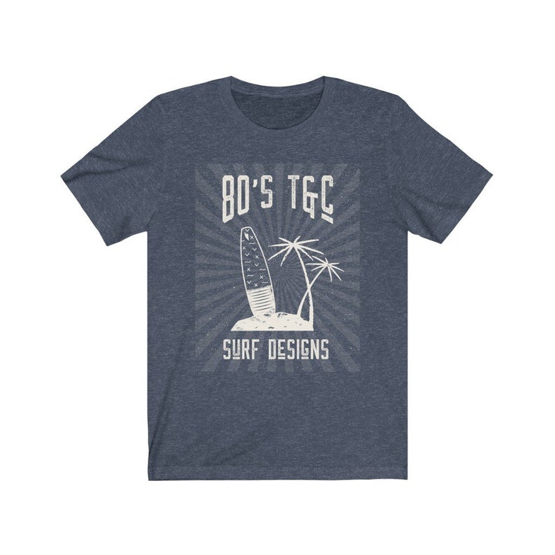 May include: A navy blue t-shirt with a white graphic design of a surfboard and palm trees. The graphic includes the text "80's TGC Surf Designs".