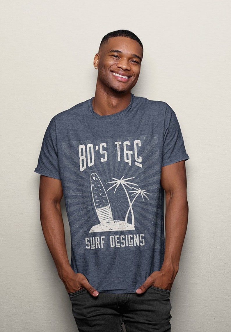 May include: A dark blue t-shirt with a white graphic design featuring a surfboard, palm trees, and the text "80's TGC Surf Designs".