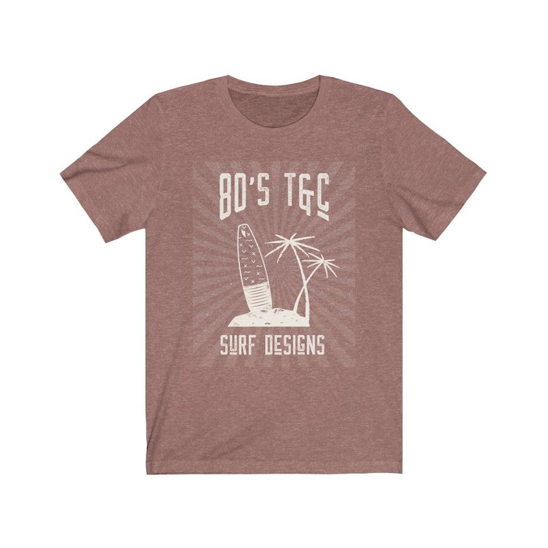 May include: A heather brown t-shirt with a vintage-style graphic of a surfboard and palm trees. The text "80's TGC Surf Designs" is printed on the shirt.