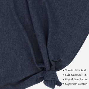 May include: Close-up of a dark blue t-shirt fabric with a knotted section. The text on the image reads: "Double Stitched", "Side-Seamed Fit", "Taped Shoulders", "Superior Cotton".