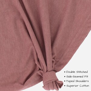 May include: Close-up of a mauve-colored t-shirt fabric with a knotted section. The fabric is described as double stitched, side-seamed fit, taped shoulders, and superior cotton.