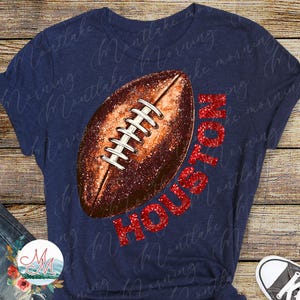 K&ouml;nnte beinhalten: Marineblaues T-Shirt mit einem Football-Design und dem Wort "HOUSTON" in rotem Glitzer. Der Football ist braun mit wei&szlig;en Schn&uuml;rsenkeln. Ein l&auml;ssiges T-Shirt f&uuml;r Sportfans.