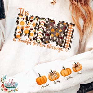 May include: White long-sleeved sweatshirt with the text "This MIMI is thankful for her blessings." The word MIMI is decorated with fall-themed patterns. The sleeve features pumpkin illustrations with names below them.