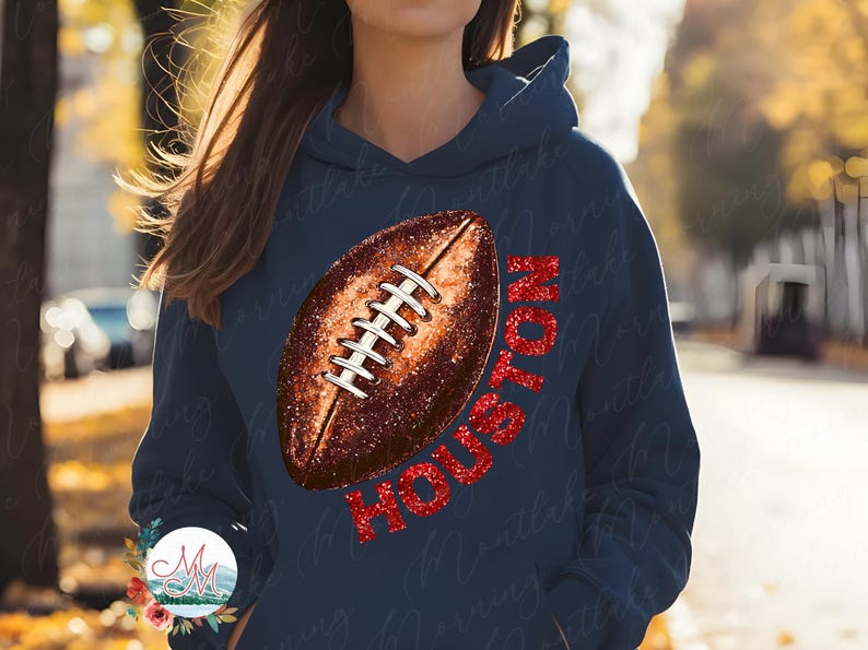 K&ouml;nnte beinhalten: Marineblauer Hoodie mit einem Football-Design und dem Wort "HOUSTON" in rotem Glitzer. Der Football ist braun mit wei&szlig;en Schn&uuml;rsenkeln. Ein l&auml;ssiges, sportliches Kleidungsst&uuml;ck.