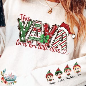 May include: White long-sleeved sweatshirt with a Christmas-themed graphic. The design features the word "YAYA" in festive colors and patterns, a Santa hat, and the phrase "loves her little elves." Below are four elf faces with names.