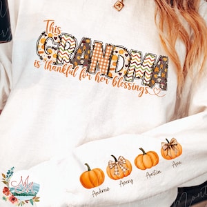 May include: White long-sleeve sweatshirt with the text "This GRANDMA is thankful for her blessings." The word GRANDMA is decorated with fall patterns. The sleeve features pumpkin illustrations with names: Andrew, Avery, Austin, and Ava.