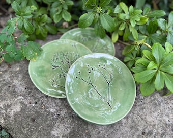 May include: Three green ceramic plates with a black floral design. The plates are stacked on top of each other.