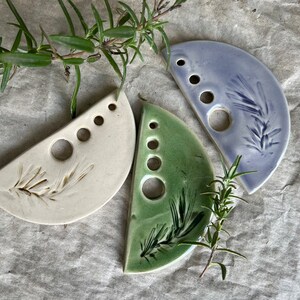 Puede incluir: Tres piezas de vajilla de cer&aacute;mica en forma de semic&iacute;rculo con un dise&ntilde;o de hojas. Cada plato tiene cinco agujeros y est&aacute; esmaltado en un color diferente: blanco, verde y azul claro.