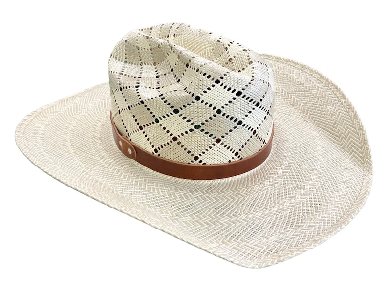 May include: A white straw cowboy hat with a brown leather band and a diamond-shaped pattern. The hat has a wide brim and a slightly pointed crown.