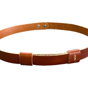 May include: A brown leather belt with a simple buckle design. The belt is adjustable and has a minimalist aesthetic.
