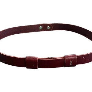 May include: A burgundy leather belt with two adjustable buckles. The belt is made of a soft, supple leather and has a simple, classic design.