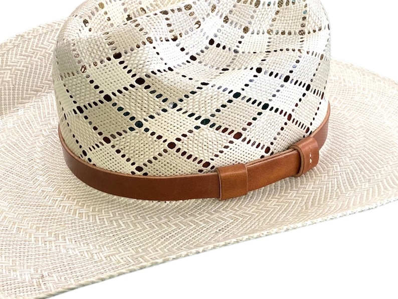 May include: A white straw cowboy hat with a brown leather band. The hat has a woven pattern and is made of a lightweight material.