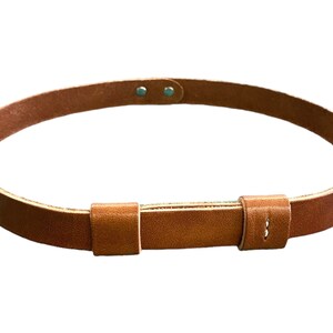 May include: A brown leather belt with a buckle and two metal rivets. The belt is made of a thick, durable leather and has a simple, classic design.