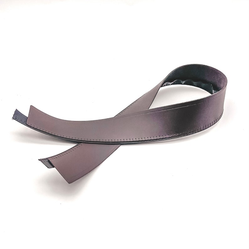 May include: A brown leather guitar strap with stitching detail. The strap is folded in half and the ends are overlapping.