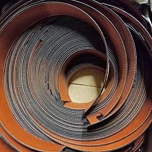 May include: Close-up of a roll of brown leather trim with a black stitching detail. The leather is rolled up in a spiral shape, revealing the stitching on the edges.