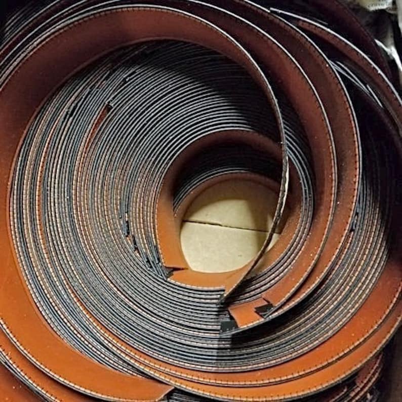 May include: Close-up of a roll of brown leather trim with a black stitching detail. The leather is rolled up in a spiral shape, revealing the stitching on the edges.