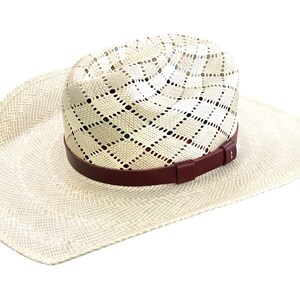 May include: A white straw cowboy hat with a brown leather band. The hat has a woven pattern and a wide brim.