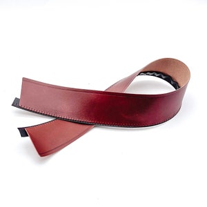 May include: A brown leather trim with a stitched edge and a black backing. The trim is folded in half and is ready to be used for a craft project.
