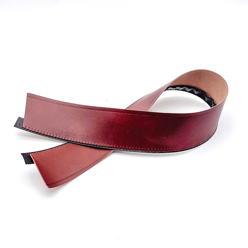 May include: A brown leather trim with a stitched edge and a black backing. The trim is folded in half and is ready to be used for a craft project.