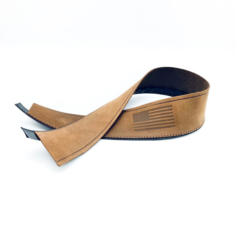 May include: A brown leather strap with a stitched edge and an American flag design. The strap is folded in half and the flag is visible on the top half.