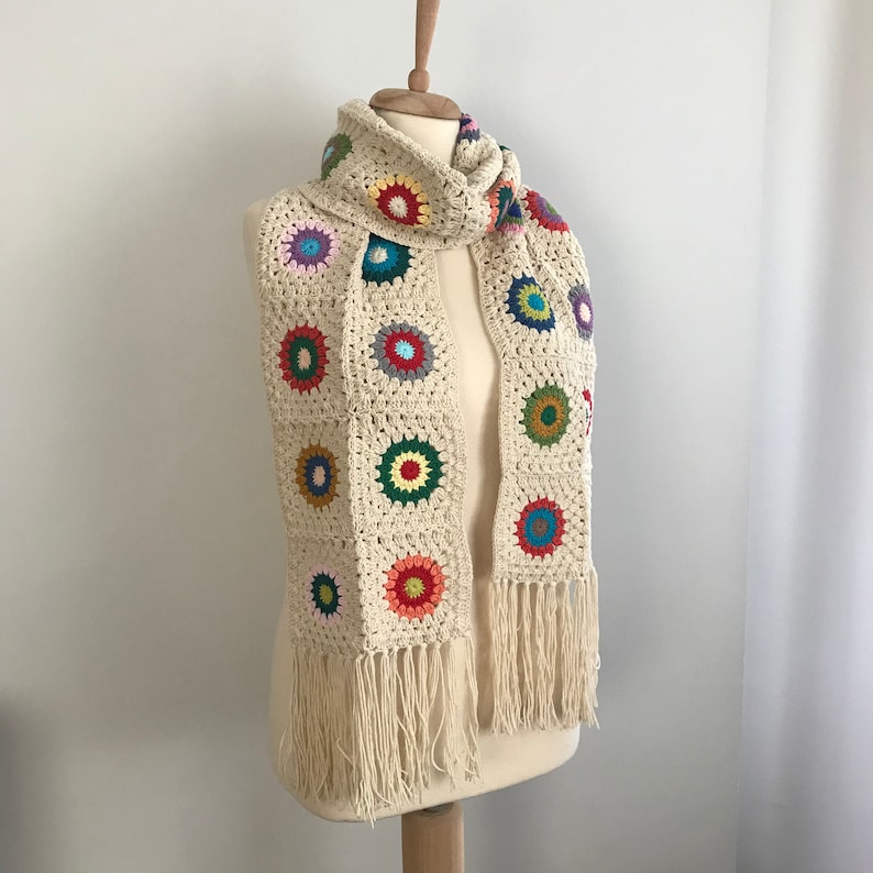 May include: A crocheted scarf with a fringe, featuring a white background with colorful circular designs.
