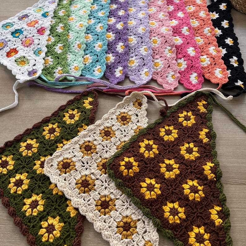 May include: A collection of crocheted triangle scarves with floral patterns. The scarves are in various colors, including green, brown, white, and pink. The scarves are made with a daisy-like flower pattern.