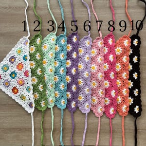 May include: A collection of ten crocheted triangle tops in various colors, each adorned with daisy patterns. The tops are numbered 1 through 10, with colors ranging from white to black, including green, purple, and pink.